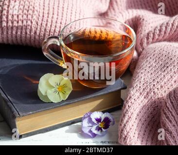 Cup of tea, book and flowers on light wooden background. Reading concept.