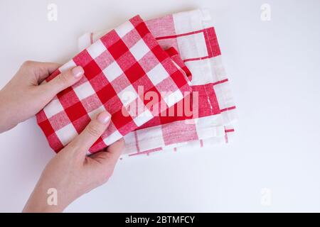 Woman hands holding red checkered kitchen towels. Two folded red and white tablecloth in female hands on white background. Stock Photo