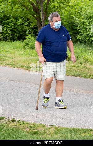 A middle aged Asian America man out for an exercise walk using a cane & wearing a surgical mask. In Little Bay Park, Whitestone, Queens, New York City Stock Photo
