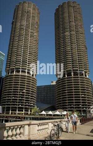 Vertical shot of a parked bicycle and a young couple strolling over the State St Bridge in front of the Marina City towers on a sunny day, Chicago Stock Photo