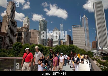 Horizontal lateral close up view of some people crossing the Renzo Piano Nichols Bridgeway, with the Chicago skyline as background, Millenium Park Stock Photo