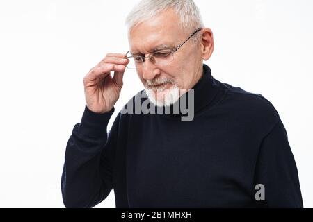 Old attractive man with gray hair and beard in eyeglasses and sweater thoughtfully looking aside while spending time over white background Stock Photo