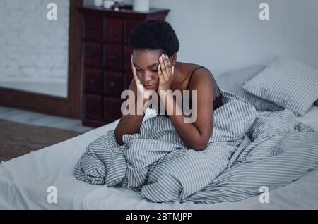 Girl woke up at night, sitting on bed and holding her hands to head Stock Photo