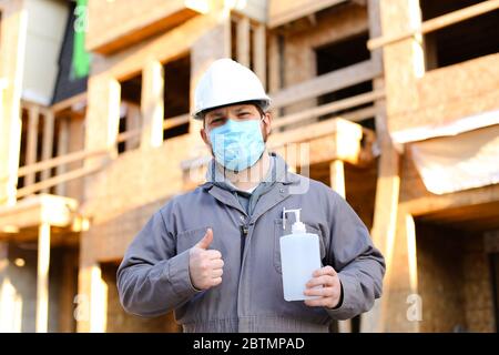 Engineer wearing mask and hardhat showing thumbs up and disinfectant. Stock Photo