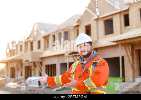 Male builder showing construction site, building in background. Stock Photo