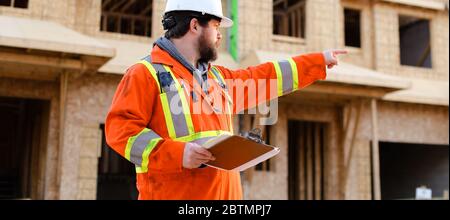 Banner of builder in orange workwear holding notebook on construction site. Stock Photo