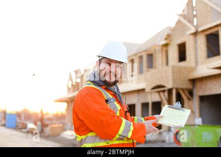 American foreman in orange workwear holding notebook on construction site. Stock Photo