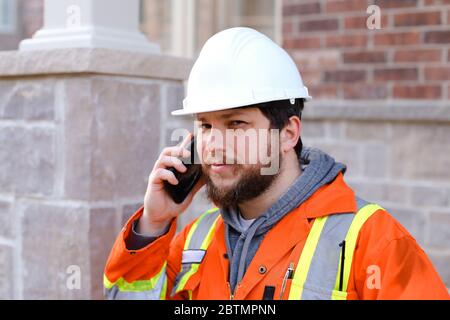 Portrait of foreman or builder in hardhat talkign by smartphone outside. Stock Photo