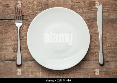Empty white plate with knife and fork on a wooden table. Stock Photo