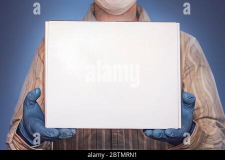 Concept of delivery goods during quarantine 2019-ncov. Young man in medical mask and blue gloves holds cardboard box in hands. Contactless delivery Stock Photo