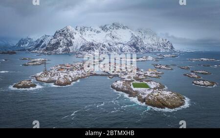 Famous footbal playfield at rocky island in far north. Distant mountains covered with snow. Green football pitch and fishing village of Henningsvaer i Stock Photo