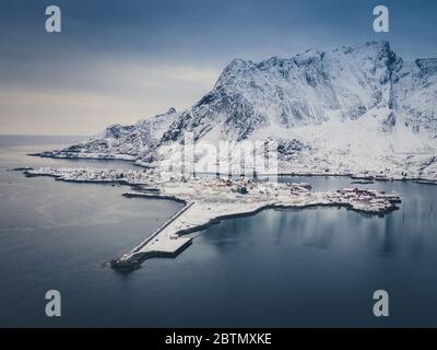 Winter morning at tranquil fishing village of Reine, Lofoten, Norway. Steep mountains covered with snow rise over cold waters of fjord ant tiny fishin Stock Photo