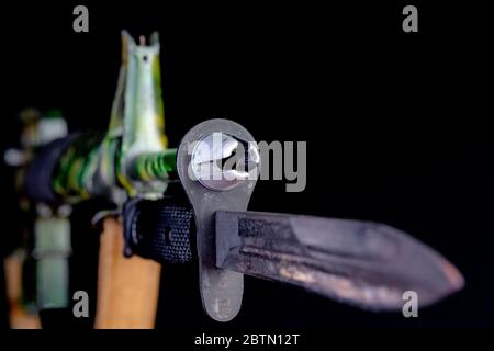 End of an assault rifle. Shallow depth of field, focus on flash suppressor. Rifle has a bayonet and is camouflage color. Black background. Stock Photo