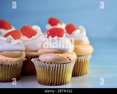 Yellow cupcakes with orange and white swirled frosting piled high and an orange gum drop candy on top.  Orange creamsicle cupcake, delicious baked goo Stock Photo