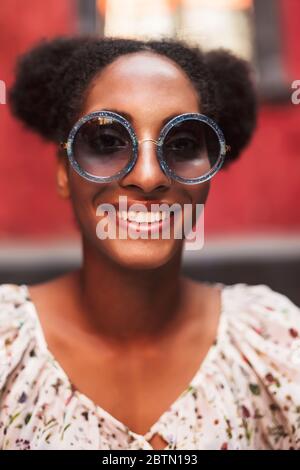 Portrait of beautiful smiling african girl with dark curly hair in sunglasses happily looking in camera Stock Photo