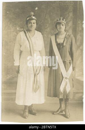 Photographic postcard of Magdalene Hendricks and sister in Eastern Star regalia. Black and white photographic postcard of Magdalene Hendricks (right) and her sister (left) wearing tiaras and sashes across their right shoulders. Magdalene Hendricks is wearing is a dark colored, mid-calf length dress with a loose drop waist, long sleeves and a square neckline. Stock Photo