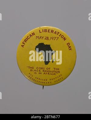 Pinback button promoting African Liberation Day. Round pin-back button with black silhouette image of Africa at center. Button has red type set against a yellow background. Type reads, [AFRICAN LIBERATION DAY/MAY 28, 1977/'THE CORE OF THE/BLACK REVOLUTION/IS IN AFRICA!'/ALL AFRICAN PEOPLES/REVOLUTIONARY PARTY]. Stock Photo