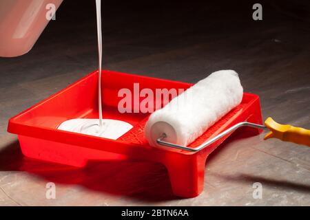 Pouring white latex paint in a tray before painting a room. Stock Photo