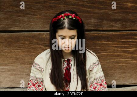 beautiful brunette woman in national ukrainian embroidery clothes on background of old native wooden house Stock Photo