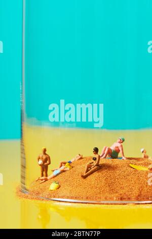 some miniature people wearing swimsuit relaxing on the sand in a bell jar, symbolizing different ideas, such as the greenhouse effect or the protectio Stock Photo