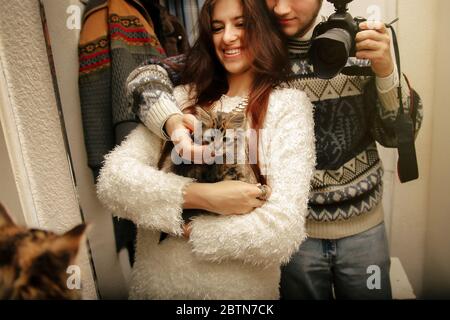 stylish hipster couple adopted homeless sweet little kitten and making selfie, first moments at home Stock Photo