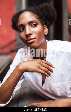 Portrait of beautiful african lady with dark curly hair in white shirt dreamily looking aside Stock Photo