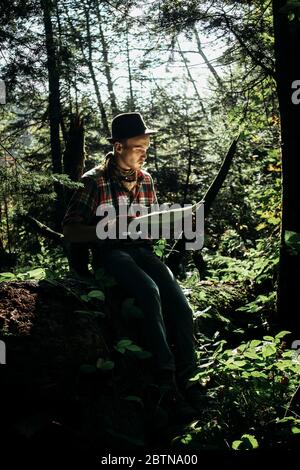 stylish hipster traveler exploring map with compass in sunny forest in the mountains Stock Photo