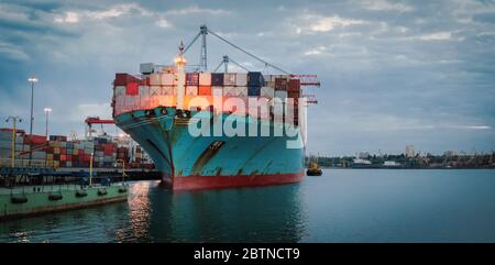 Container cargo ship load in the seaport at dusk. Logistics and transportation of Container Cargo ship with working crane bridge in shipyard, logistic Stock Photo