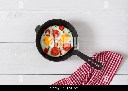 Fresh delicious breakfast of eggs and tomatoes with spices and red pepper, frying pan with fried eggs on white wooden background, top view, copy space Stock Photo