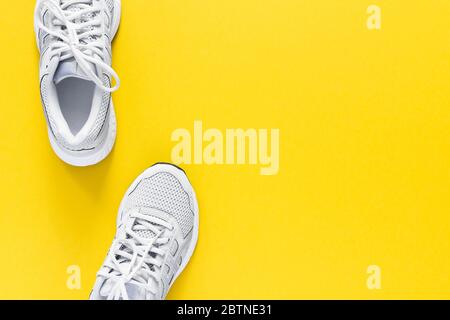 White sneakers isolated on a yellow background, seasonal shoes for walking and sports, copy space, top view Stock Photo
