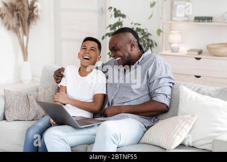 Preteen Black Boy Watching Comedy Movie On Laptop With Grandfather And Laughing Stock Photo