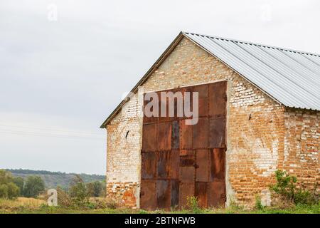 Old red brick hangar with huge gates made of rusted metal. Warehouse for rural products. Stock Photo