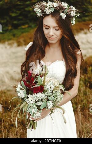 stylish bride posing with bouquet on background of forest, luxury gorgeous boho wedding at mountains Stock Photo