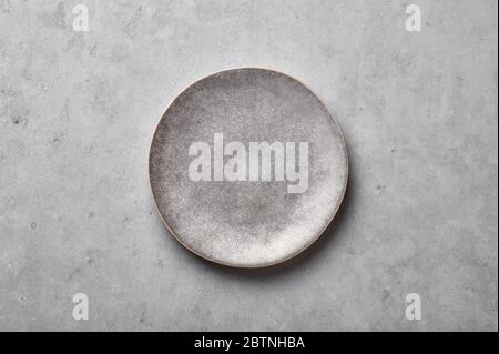 Gray ceramic plate on grey concrete rough background. Empty spotted uneven saucer. Matte dish on stone textured backdrop. Hand made ceramic table sett Stock Photo