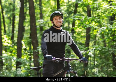 Cheerful cyclist posing with bike over forest background Stock Photo