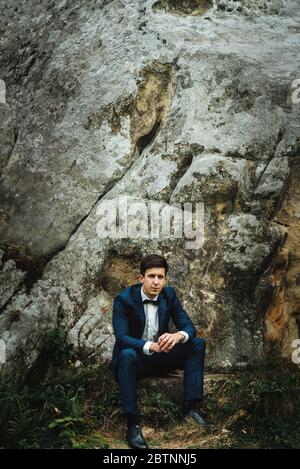 stylish elegant happy groom in fashionable suit posing on background of rocks in mountains Stock Photo