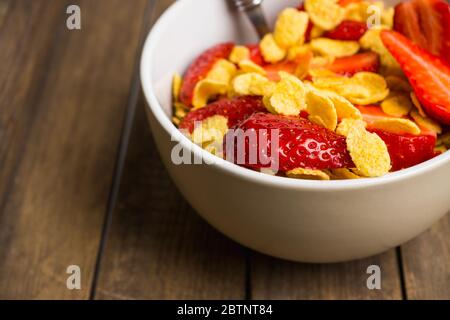 Corn flakes with fresh strawberry in bowl on the rustic background. Shallow depth of field. Stock Photo