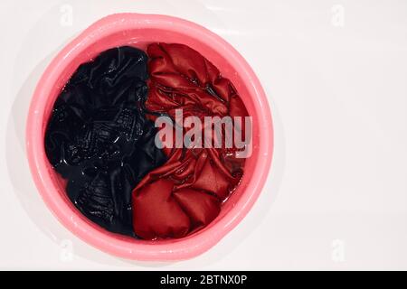 soaked dirty clothes in a red basin on a white bath. isolated Stock Photo