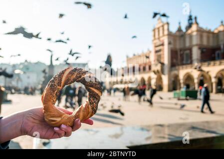 Woman holding bagel / obwarzanek / pretzel - traditional Polish snack on Market Square in Cracow.  Tourist hand holding pretzel on the Cracow Cloth Ha Stock Photo
