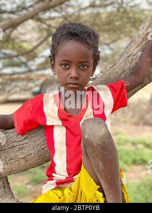 Portrait of sad little boy sitting on a tree, Danakil Depression, Afar Region, Ethiopia, Africa Stock Photo