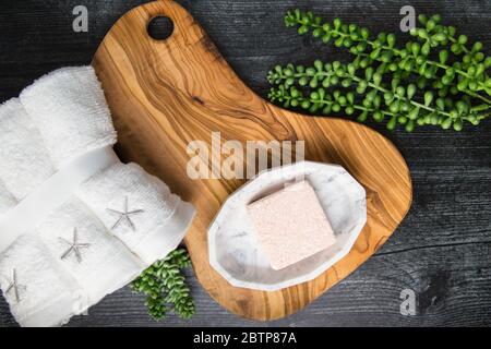 Flat lay of pink foaming bath bomb cube on wooden tray with towels and succulents  ready to be used for a relaxing spa experience Stock Photo