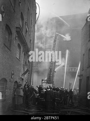 London race warehouse blaze . Carbett ' s rice warehouse in Shad Thames caught fire and blazed furiously . Photo shows , firemen directing hoses at the blazing building . 1 April 1936 Stock Photo