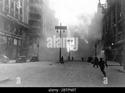 Madrid again under fire. Shell that killed three, injured 15. British women MPs in danger. This picture just received in London from Madrid, was taken by photographer in an ambulance as rebel bombs and shells rained down in the intense bombardment which the rebels are again directing on the city. People can be seen running for their lives in the Gran Via, Madrid street, as a shell hits a building on the right. This shell killed three persons and injured 15. The people running in the centre were caught by the explosion and badly hurt. This bombardment also endangered the lives of the Duchess of Stock Photo