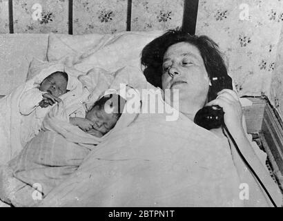 Twins born by telephone. When the twin boys of Mrs Emma Nelson arrived more quickly than she anticipated, and she found she had no time to send for a doctor, she telephone the Maternity Centre in Chicago, Illinois, where she lives, and received instruction from a surgeon at the centre as to what to do. Before a nurse could arrived to help her, the second twin arrived, and Mrs Nelson resumed her telephone contact with the Maternity Centre. Photo shows: Mrs Emma Nelson and her twins shortly after their birth at Chicago. 26 April 1937 Stock Photo