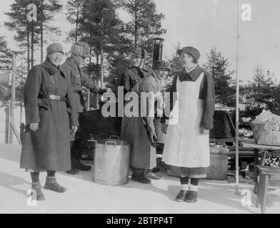 Women 'soldiers' of Finland. They cook at a Field Kitchen!. Military uniformed members of 'Lottas', the Finnish women's patriotic organisation, use a field kitchen to fulfil the feminine duty or preparing food for competitors in the world skiing Championships at Lahti, Finland. One of the women is wearing an apron over her greatcoat. 26 February 26 1938 Stock Photo