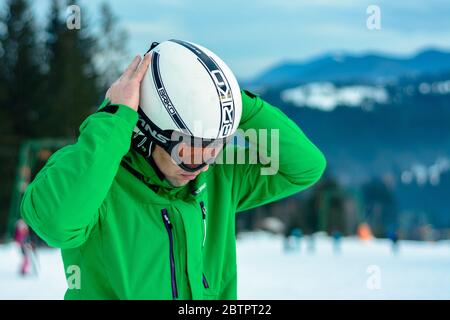 A man skier wearing a helmet briko and ski goggles swans before training for safety. A professional snowboarder prepares for competitions 2021. Yablun