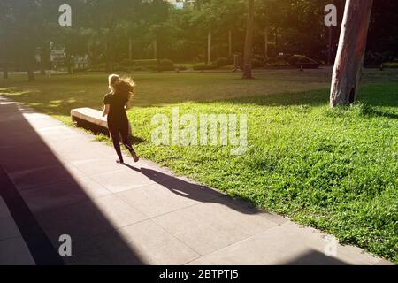 Makati, Manila, Philippines - May, 26, 2020: A girl is jogging in empty Ayala triangle park during coronavirus covid quarantine ECQ on a sunny day Stock Photo