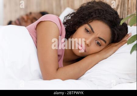 Close up of annoyed woman laying next to snoring husband Stock Photo