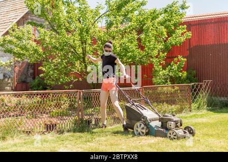 A woman in her backyard mowing grass with a lawn mower on a sunny