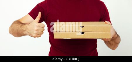 Delivery man in red t-short holding cardboard boxes of pizza on white background. Pizza delivery. Courier home delivery. food order pizza boxes Stock Photo